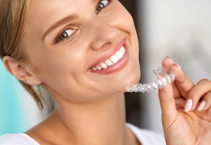 Beautiful woman holding invisalign braces and smiling at the camera