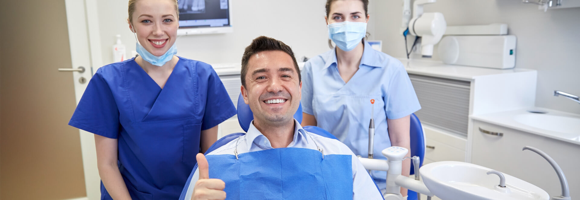 Male patient smiling showing thumbs up with dental staff behind